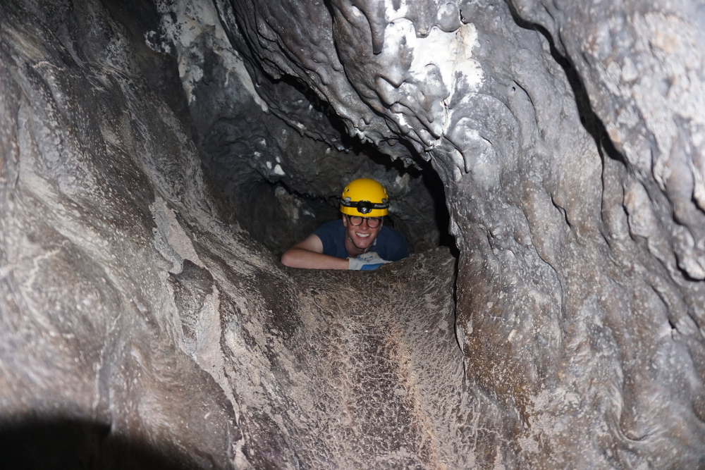 A caver coming out of the back crawl in Xenolith cave.